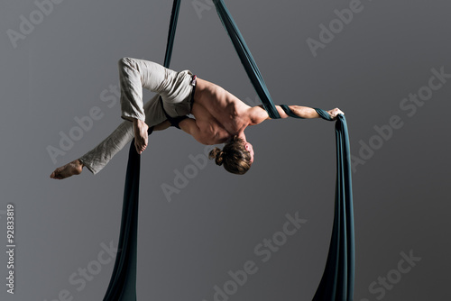 Sporty young man doing exercise with elastics, aerial silk ribbons, aerial. Sport training gym and lifestyle concept. Anti-gravity yoga.