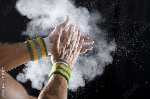 Taped hands of gymnast clapping white chalk powder into a cloud against dark background