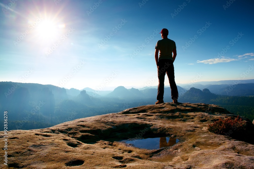 Obraz premium Alone man in red cap on peak of sharp peak in rock empires park and watching over the misty and foggy morning valley to Sun. Beautiful moment
