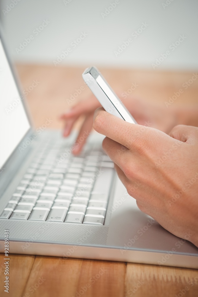 Man using mobile phone while typing on laptop Man using mobile phone while typing on laptop
