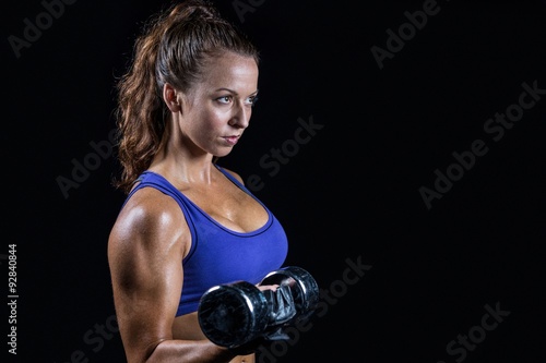 Side view of fit woman lifting dumbbell