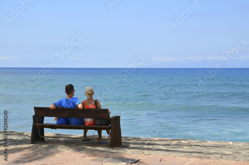 Young couple sitting on a bench by the ocean.