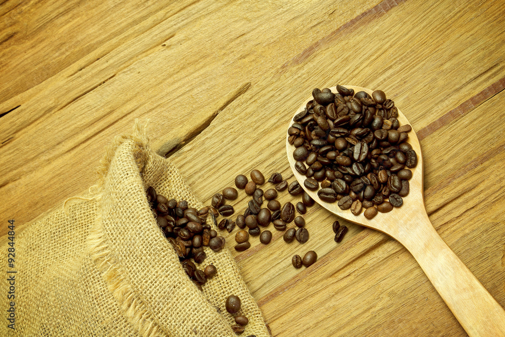 Coffee beans spilling from a burlap bag and a scoop on a texture Coffee beans spilling from a burlap bag and a scoop on a texture