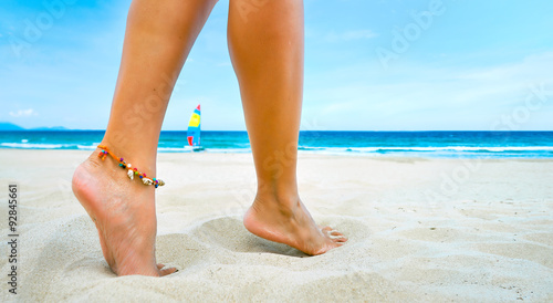 Young female legs one bracelet on sandy tropical beach