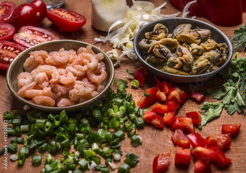 peeled shrimp and mussels with chopped pepper and green onions tomatoes on a wooden background close up