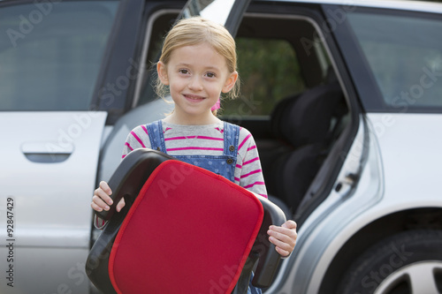 Portrait Of Girl Holding Booster Seat Standing Next To Car photo