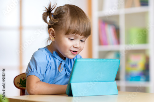 kid girl playing with tablet computer at home