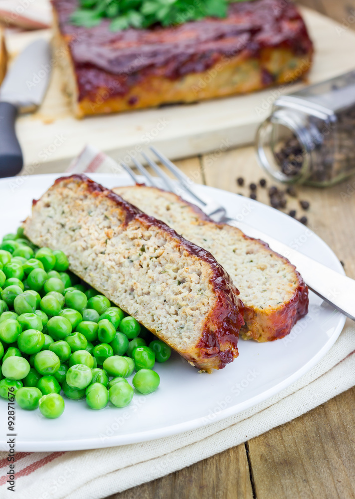 Homemade meatloaf garnished with green peas on a white plate