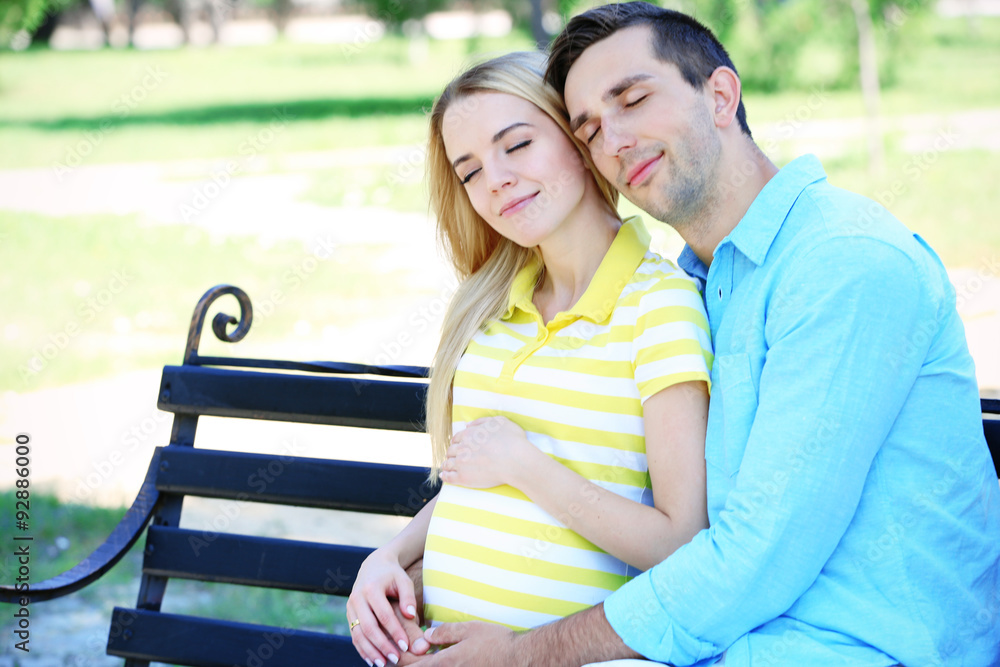 Young pregnant woman with husband sitting on bench in park Young pregnant woman with husband sitting on bench in park