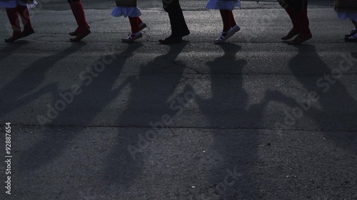 Kolo - people dancing Serbian folk dance, focus on legs and shadows on the pavement photo