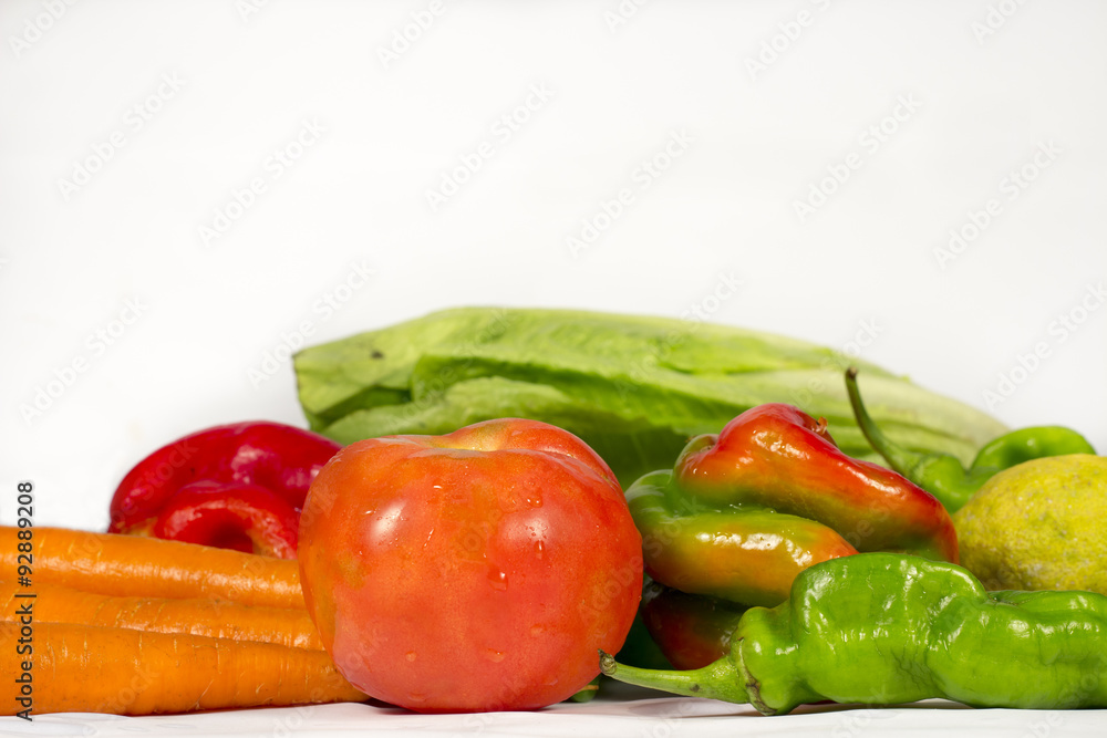 Red tomato on white, beside other vegetables and fruits, such as carrots, peppers, lettuces and lemons. Red tomato on white, beside other vegetables and fruits, such as carrots, peppers, lettuces and lemons.