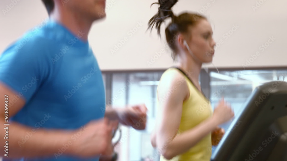 Couple running on treadmills in gym Couple running on treadmills in gym
