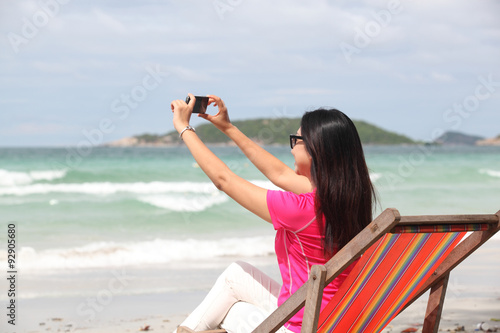Woman taking photo with cellphone on the beach on spring. Happy girl on vacation taking picture on sea background.