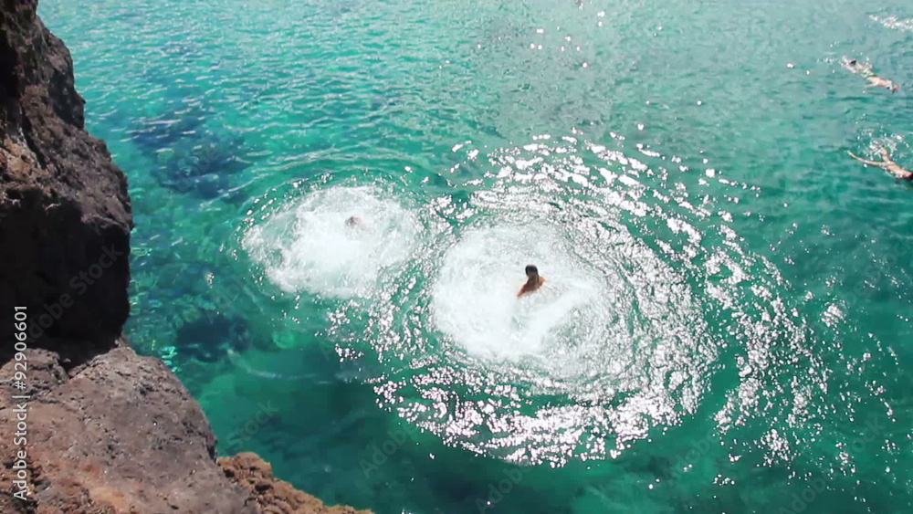 Group of friends jumping from cliff into the ocean in Hawaii. Two Girls