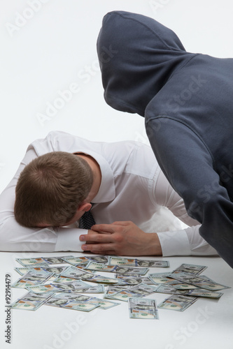 Unrecognizable robber bending over the sad businessman and money
