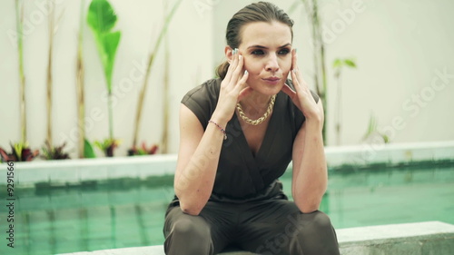 Sad, elegant woman sitting on edge of swimming pool
