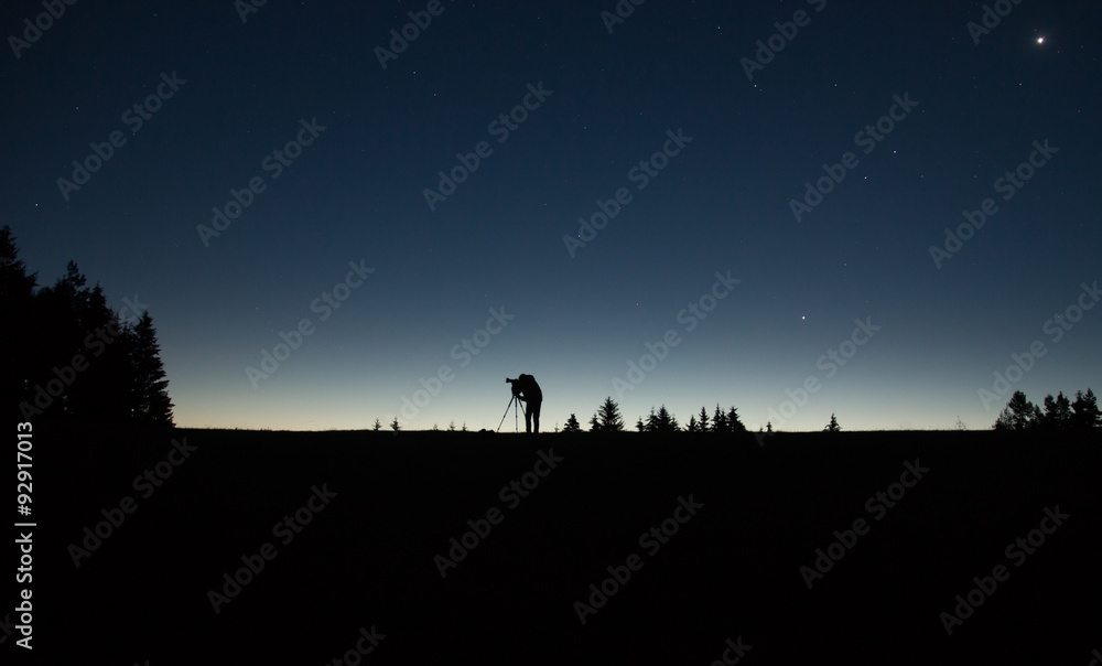 photographer silhouette with tripod standing in the night with stars