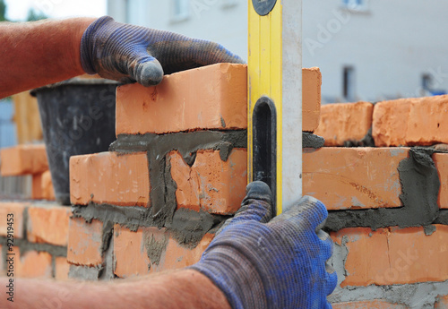 Billede på lærred Bricklayer Using a Spirit  Level to Check New  Red Brick Wall Outdoor
