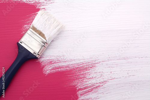Paintbrush with white paint painting over pink