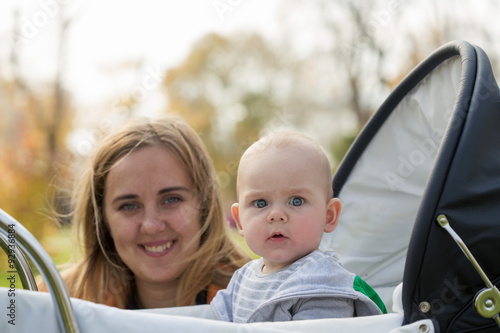 A cute little boy in a baby carriage and his mother on a background unfocused