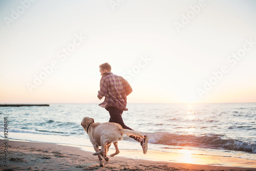 young caucasian male playing with labrador on beach during sunri