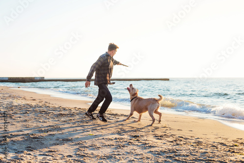 young caucasian male playing with labrador on beach during sunri