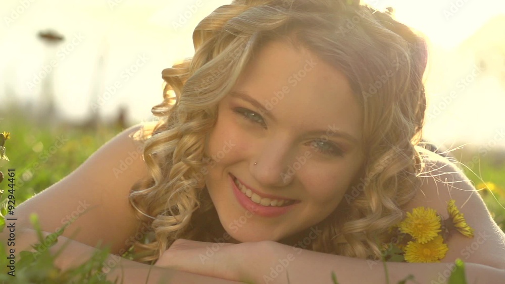 Girl lying on dandelion flowers meadow and smiling. Beautiful spring young woman Girl lying on dandelion flowers meadow and smiling. Beautiful spring young woman