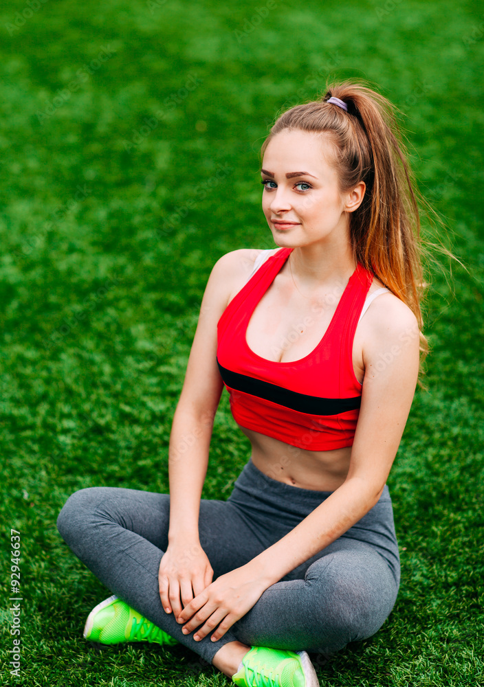 Young fitness girl sitting on green grass .
