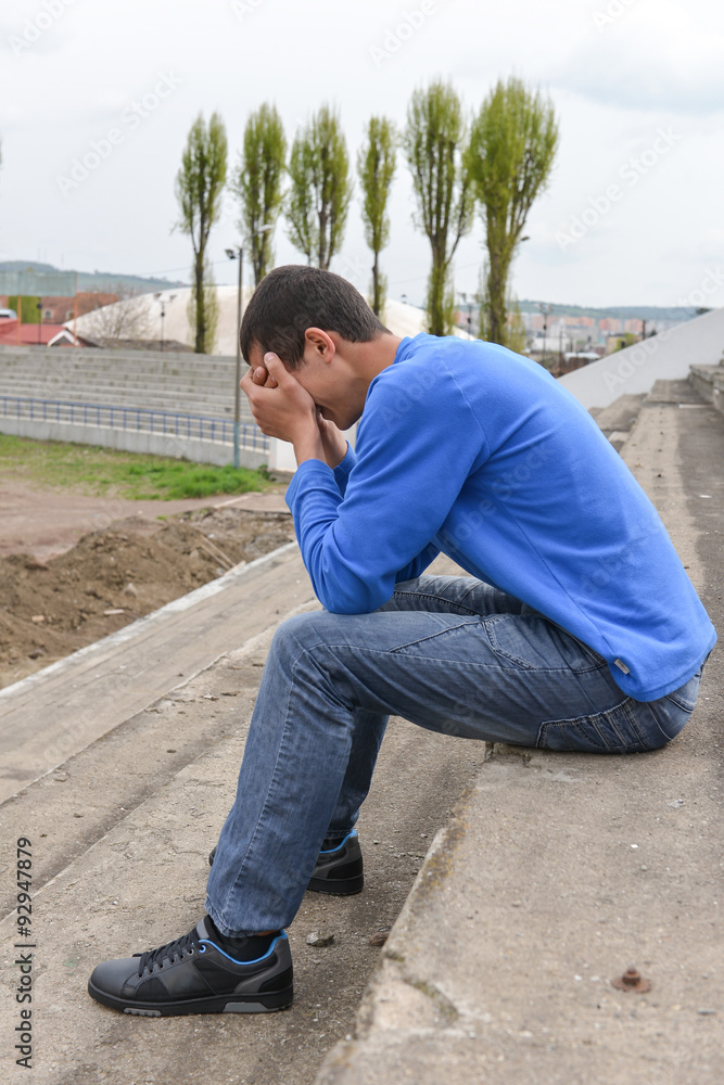 Upset teenager sitting on stairs laying his head on his hands Upset teenager sitting on stairs laying his head on his hands