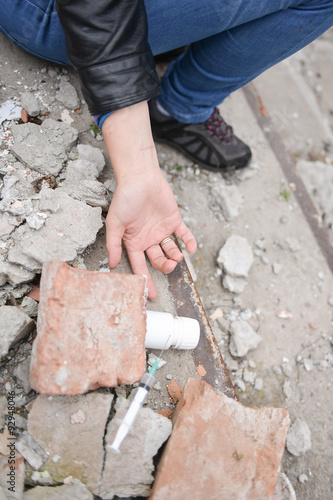 Hand of a drug addict reaching for a syringe and pills. Simulate