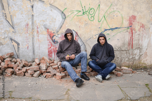Two street hooligans or rappers sitting against a graffiti paint