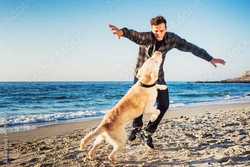young caucasian male playing with labrador on beach during sunri