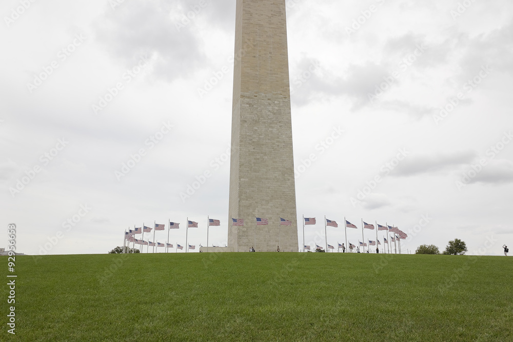View of the base of Washington DC's national monument, the Washington Monument with American flagpoles circling it's plaza, National Mall