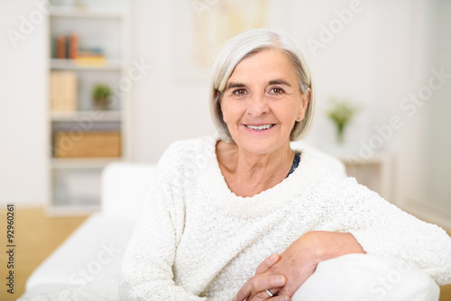 lächelnde ältere dame sitzt entspannt zuhause auf dem sofa