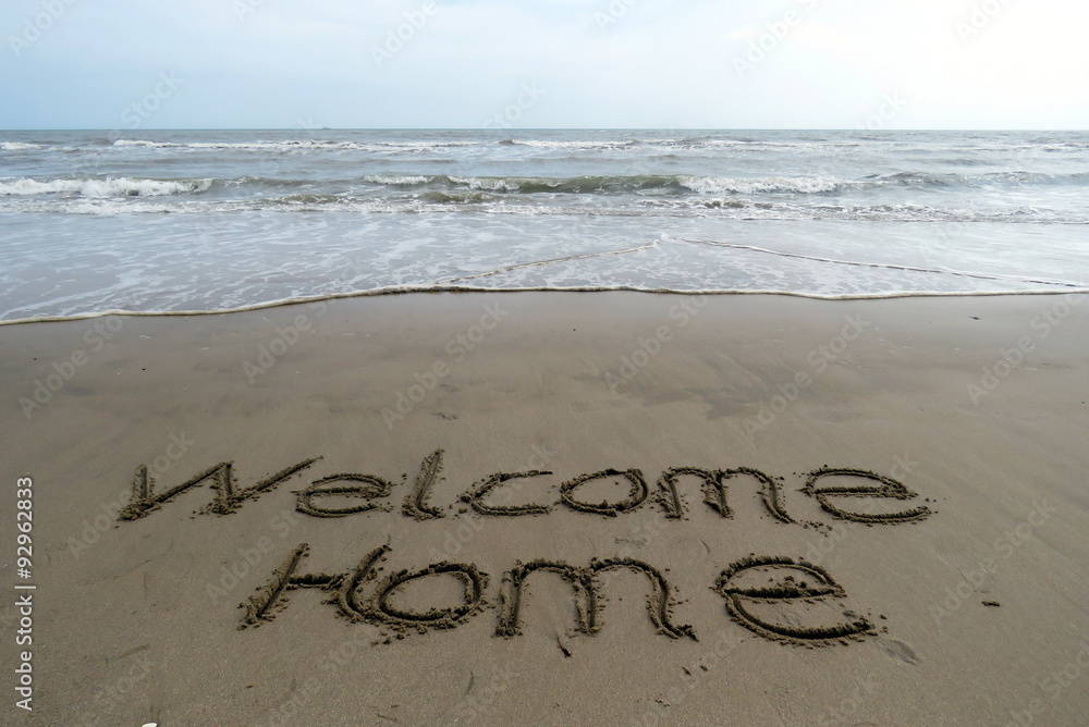 Fototapeta premium welcome home written in sand, with the sea in the background