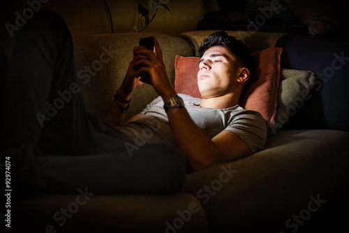 Fotografie Young Man on Sofa Lit by Light from Cell Phone
