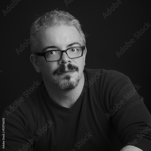 Ritratto in bianco e nero di uomo giovane con occhiali da vista, pizzetto e baffi neri photo