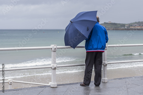 Hombre con paraguas y chaqueta azul frente al mar
