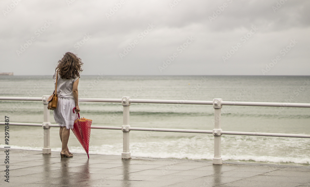 Mujer con bolso y paraguas rojo frente al mar Stock Photo | Adobe Stock