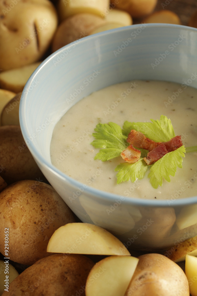 Close up of a potato soup in a pale blue bowl surrounded by potatoes Close up of a potato soup in a pale blue bowl surrounded by potatoes