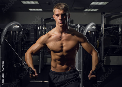 Young athletic man pumping up muscles on crossover