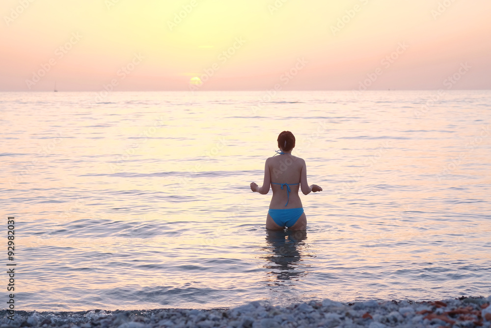 Girl stands in the sea at a sunset
