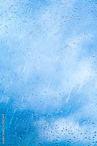 Obraz na płótnie Drops of rain on blue glass background. The sky with clouds on background. w salonie