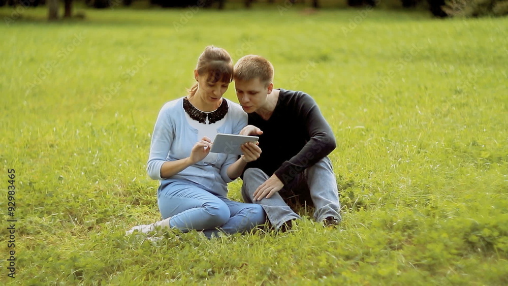 Young couple using tablet computer touchscreen in park Young couple using tablet computer touchscreen in park