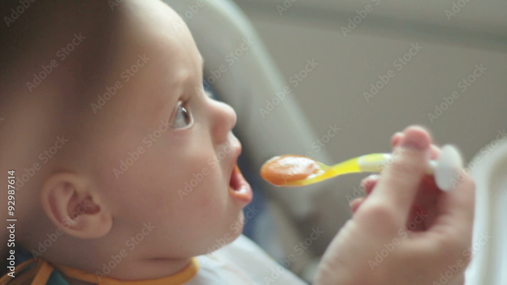 Baby sits at a children's chair. Mother feeds the child Baby sits at a children's chair. Mother feeds the child