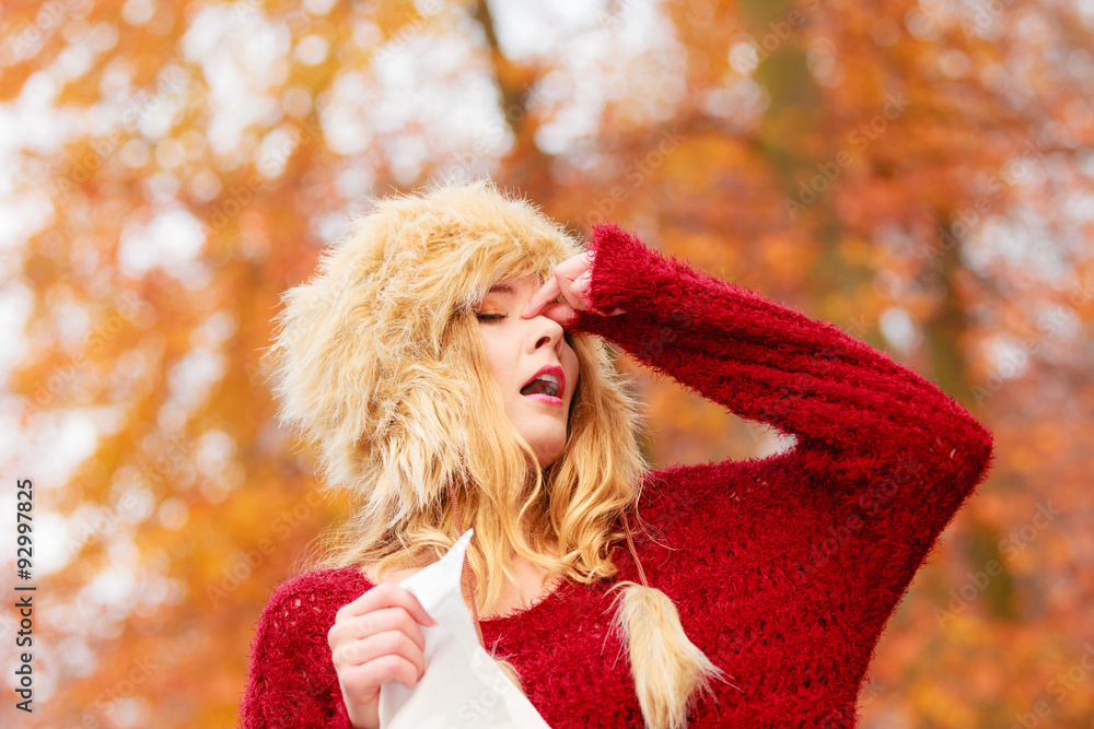 Sick woman in autumn park sneezing into tissue. Sick woman in autumn park sneezing into tissue.