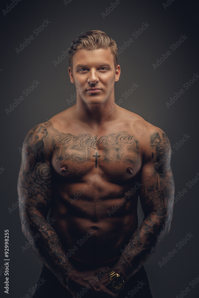 Fototapeta premium Portrait of muscular tattooed man in shadows isolated on grey background.