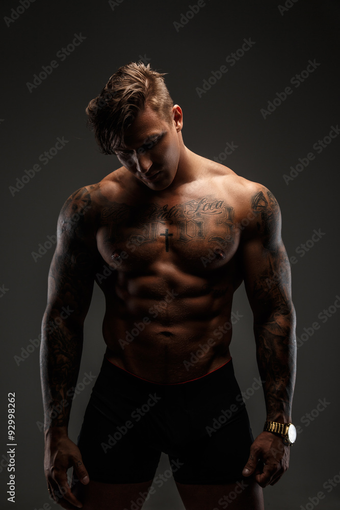 Portrait of muscular tattooed man in shadows isolated on grey background. Portrait of muscular tattooed man in shadows isolated on grey background.