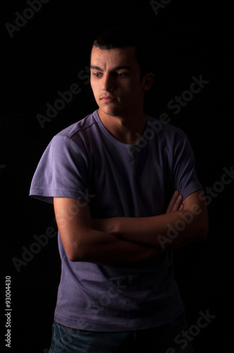 Serious young man standing with arms crossed on black background