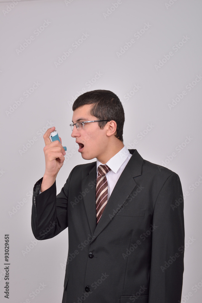 Young caucasian man in suit using an asthma inhaler to handle pr Young caucasian man in suit using an asthma inhaler to handle pr